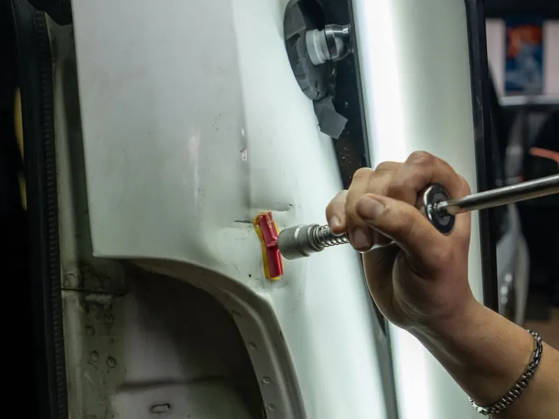Técnico reparando una abolladura en la carrocería con herramienta especial