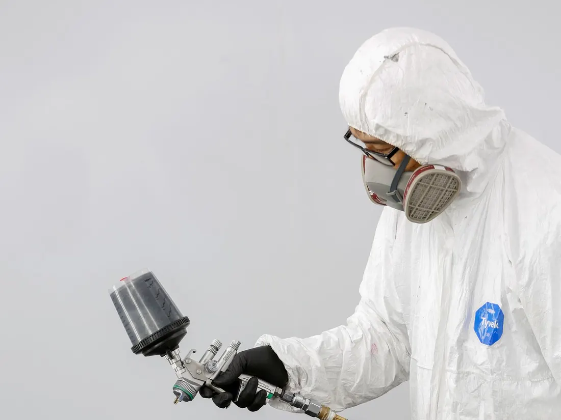 Pintor con traje de protección aplicando pintura con pistola sobre una defensa