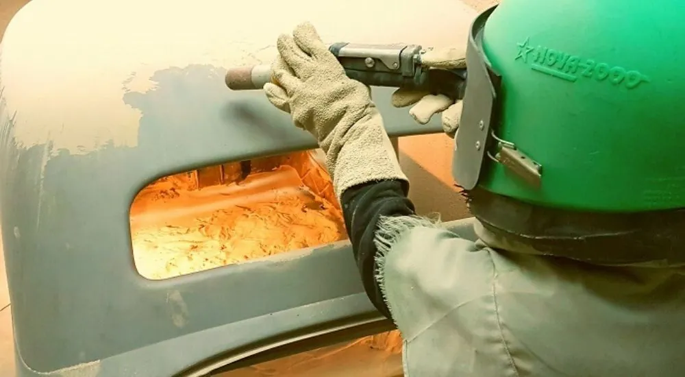 Técnico decapando la pintura de una carrocería con equipo de arenado